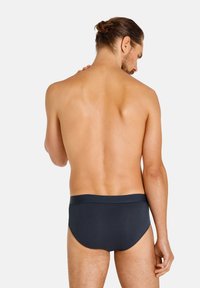 Slip blu scuro con una morbida fascia in vita, tessuto liscio e design aderente, mostrati da dietro su un torso nudo.