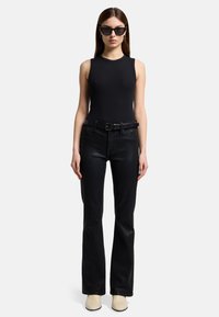 Czarny prążkowany top bez rękawów zestawiony z dopasowanymi czarnymi skórzanymi spodniami rozszerzanymi i czarnym paskiem; uzupełniony beżowymi butami na obcasie i okularami przeciwsłonecznymi.