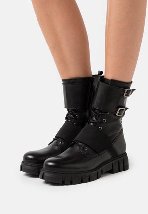 Bottes courtes en cuir noir à finition mate, avec un bord rembourré, des boucles ajustables et des semelles épaisses en caoutchouc. Modèle à lacets.