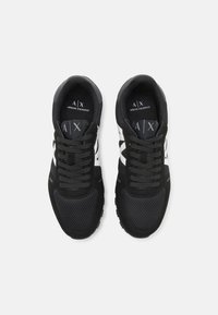 Baskets de sport noires en maille et daim, avec des lacets, un logo blanc et des semelles en caoutchouc texturé.