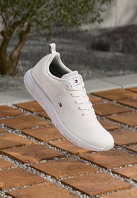 Weißer Sport-Sneaker aus gestricktem Material, mit strukturierten Streifen, Schnürung und einem kleinen Markenlogo auf der Zunge.