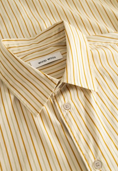 Raidallinen paita, jossa kermanvärinen pohja ja keltaisen kultaiset sekä vihreät raidat. Paidassa on klassinen kaulus, napitus edessä ja etiketti, jossa lukee "WOOD WOOD".