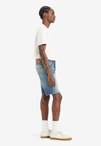 Shorts in denim di colore azzurro chiaro con lavaggio sbiadito e orlo grezzo, abbinati a una maglietta bianca a maniche corte e sneaker crema con dettagli marroni.