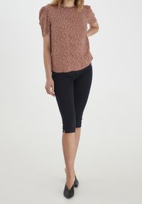 Blusa rossa e crema a fantasia con maniche a palloncino corte, abbinata a pantaloni blu scuro alla lunghezza del ginocchio. Scarpe nere a punta completano l'outfit.