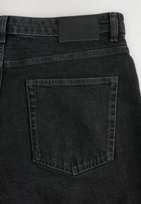 Jeans negri din denim cu o finisare texturată, având un singur buzunar la spate și o etichetă din piele neagră deasupra acestuia. Cusături curate și un design modern.