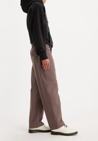 Tmavě šedá mikina, volné béžovo-hnědé kalhoty a bílé boty s černými akcenty. Tkanina vypadá pevně a má hladký povrch.