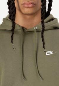 Φούτερ Nike σε ελιά πράσινο με κορδόνι. Διαθέτει λευκό λογότυπο στο στήθος. Μαλακό, υφασμάτινο ύφασμα με άνετη εφαρμογή.