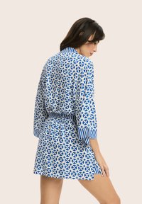 Niebieska i biała sukienka w geometryczny wzór, z paskiem w talii i paskowanymi mankietami. Lekka tkanina, do długości nad kolano.