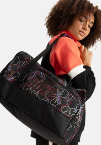 Black duffel bag with colorful floral pattern and red text "ROXY." Features sturdy straps and contrasting black and colored fabric sections.