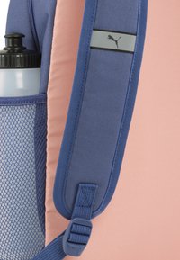 Zaino blu e rosa con una tasca laterale in rete per una bottiglia d'acqua, fascia grigia con logo e supporto per cinturino regolabile.
