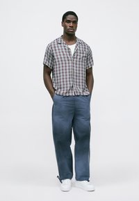 Burgundinės ir baltos spalvos kvadratiniais raštais trumpomis rankovėmis marškiniai, derinami su laisvomis mėlynomis kelnėmis ir baltomis sportbačiais. Paprastas ir kasdieniškas dizainas.