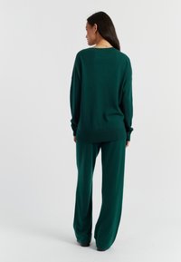 Un pull en tricot teal avec une coupe décontractée, des manches longues et un col rond, associé à un pantalon large assorti dans le même matériau et la même couleur.