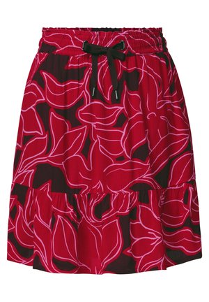 Jupe rouge avec de grands motifs floraux rouge foncé, dotée d'un cordon noir à la taille, portée avec un top blanc et une veste en jean claire.