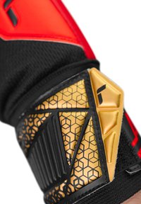 Guanto sportivo nero e rosso con un cinturino per il polso in tessuto testurizzato oro e nero che presenta un motivo esagonale e dettagli in gomma.