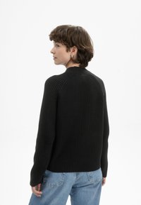 Schwarzer gerippter Pullover mit Rundhalsausschnitt, enganliegenden langen Ärmeln und Rückennähten, kombiniert mit hellblauen hochtaillierten Jeans.
