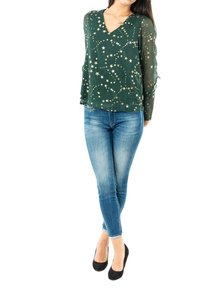 Grön långärmad blus med V-ringning och stjärnmönster; kombinerad med blå slim fit-jeans och svarta högklackade skor.