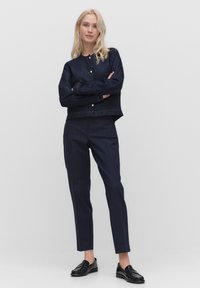 Donkerdenim cropped jack met gouden knopen, gecombineerd met marineblauwe gestreepte broek en zwarte instapschoenen. Soepele textuur, getailleerde pasvorm.