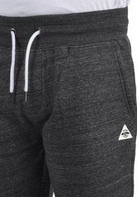 Pantalones de chándal grises con una tela texturizada, que cuentan con un cordón blanco, cintura elástica, bolsillos laterales y una etiqueta de logo triangular.