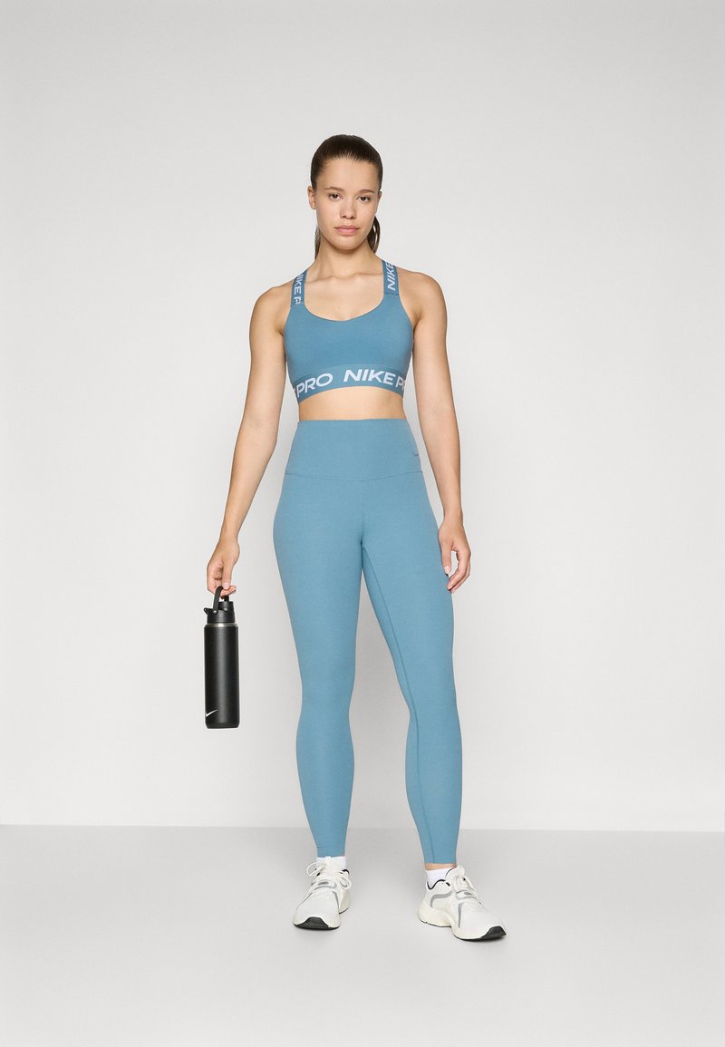 Helles blaues Sport-BH mit "PRO NIKE"-Bande, passende hochgeschnittene Leggings und eine schwarze Wasserflasche. Weiße Schuhe mit schwarzen Akzenten.