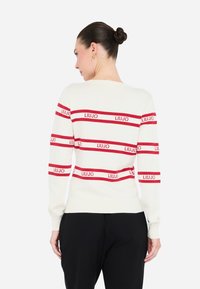 Maglione a maniche lunghe crema con righe orizzontali rosse che presenta la scritta "LIU-JO." Tessuto a maglia morbida, design aderente. Polsini e orlo a coste a contrasto.