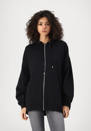Black zip-up hoodie with large pockets, oversized fit, and drawstring hood. Soft fabric with ribbed cuffs and hem, featuring a smooth texture.
