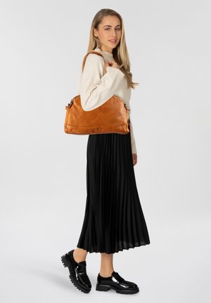 Borsa a tracolla in pelle color tan con design strutturato, dotata di chiusura con zip e manici corti. Il modello indossa un maglione color crema e una gonna a pieghe nera.