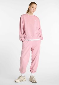 Sweatshirt rose et joggings assortis en tissu doux. L'ensemble présente un petit logo sur la poitrine et des chevilles rétrécies.