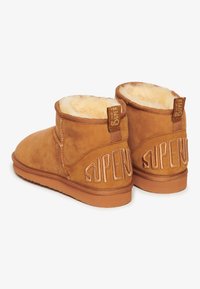 Botas cortas de ante marrón con forro interior esponjoso, que presentan el logotipo bordado "SUPER" en la parte trasera y una suela de goma plana.