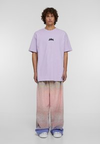 Lavendel bomulls t-skjorte med korte ermer, med en liten svart grafikk. Vide bukser i en pastellgradiant av rosa og blå.