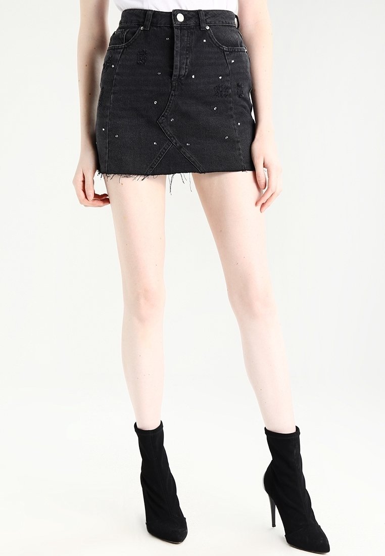 Svart denimminikjol med fransig fåll, med silverstuddar och en distinkt snedställd framdesign, hög midja.