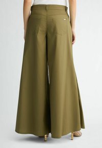Pantalons larges vert olive avec une texture lisse, deux poches à l'arrière et des fentes sur les côtés. Présente une taille sécurisée et un style minimaliste.