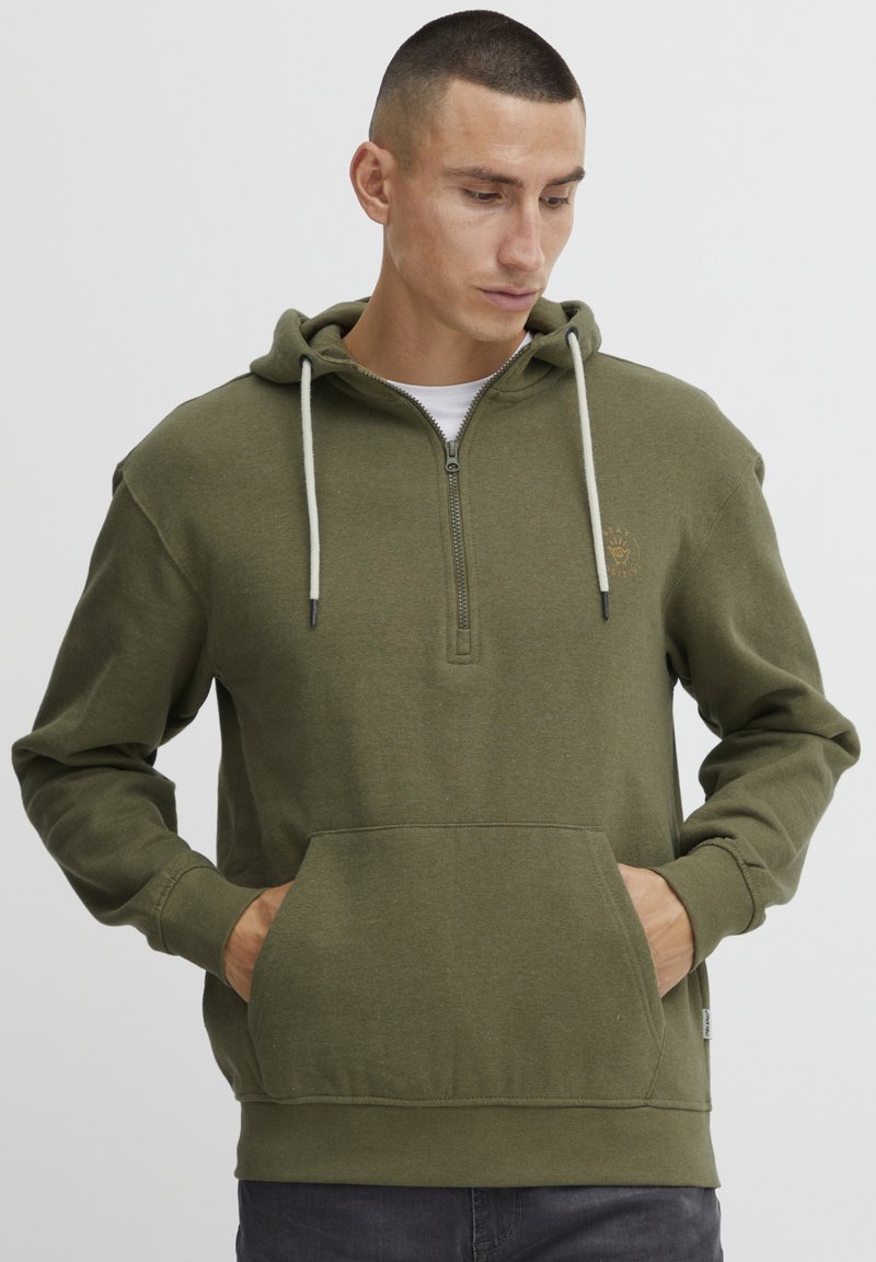 Felpa con zip verde oliva, dotata di tasca a marsupio, cappuccio regolabile con cordino e polsini a coste. Presenta un piccolo logo sopra la tasca. Materiale morbido.