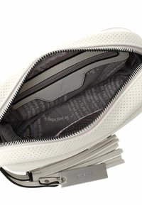 Interno di una borsa a tracolla bianca perforata con una fodera scura a motivo, tasca con zip e un'etichetta che riporta "SURI FREY." Superficie testurizzata e design lungimirante.