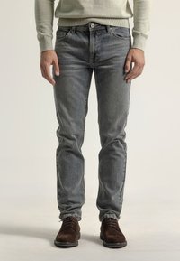 Jeans ajustados de color azul en denim desgastado con un diseño clásico de cinco bolsillos. Combinados con zapatos de ante marrón, mostrando un look informal.