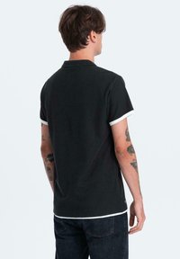 Zwart poloshirt met contrasterende witte manchetten, korte mouwen en een schoon, eenvoudig ontwerp. De stof lijkt zacht met een gladde textuur.
