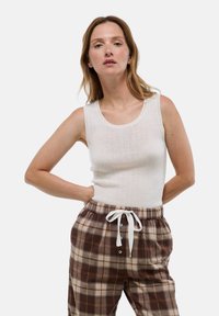 Débardeur blanc à côtes avec un col rond, associé à un pantalon carreauté marron et beige avec une taille élastique et un cordon de serrage.