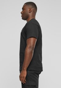 Sort bomulds T-shirt med korte ærmer og rund hals, der har et logografik på forsiden. Siden viser en afslappet pasform og glat tekstur.