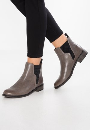 Bottes chevilles en cuir gris avec des panneaux élastiques sur les côtés, un petit talon carré et un accent texturé sur les côtés. Portées avec un pantalon noir ajusté.