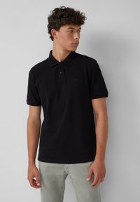 Zwart poloshirt gemaakt van katoen, met een klassieke kraag, korte mouwen en een subtiele logo op de borst, gecombineerd met lichtgrijze broeken.