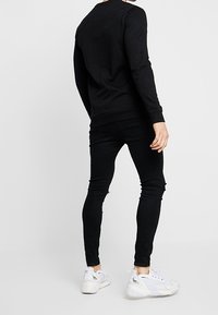 Musta pitkähihainen collegepaita, kapealahkeiset mustat farkut, joissa on rispaantuneisuutta, ja valkoiset urheilulliset tennarit. Yksinkertainen, yksivärinen asukokonaisuus.