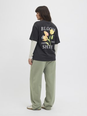 Czarna koszulka z kolorową grafiką tulipana i napisem "BLOOM & SHINE" na plecach, w połączeniu z jasnooliwkowymi, luźnymi spodniami.