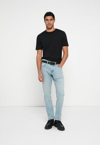 Czarny t-shirt z krótkim rękawem zestawiony z jasnoniebieskimi dżinsami i czarnymi butami. Strój uzupełnia czarny pasek z srebrną klamrą.