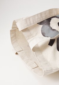 Canvas bag with a grey floral pattern. Features a soft, textured surface and sturdy, flat handles. Neutral beige color.