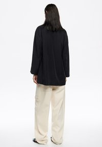 Camicia nera a maniche lunghe con una vestibilità ampia, apertura sul retro e tessuto liscio, abbinata a pantaloni panna a gamba larga con tasche laterali.