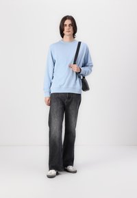 Lichtblauwe sweatshirt, zwarte schoudertas, donkergrijze flared jeans en witte sneakers. Glad materiaal, casual ontwerp, relaxte pasvorm.