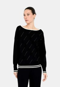 Maglione nero con un ampio scollo a barca, caratterizzato da linee diagonali e piccoli dettagli. Maniche e fondo a costine con righe bianche. Tessuto testurizzato.