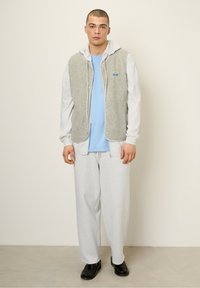 Fleece vest in light gray, layered over a blue long-sleeve shirt. Loose gray sweatpants and black shoes complete the outfit.