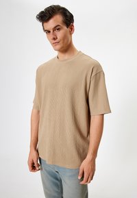 Beige tekstureret t-shirt med rund halsudskæring og korte ærmer, parret med lyseblå denim jeans. Stoffet har en ribbet overflade.