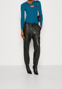 Blauwe geribde lange mouw top met een uitsnijding aan de voorkant, gecombineerd met zwarte faux leren joggers en zwarte puntige enkellaarsjes.