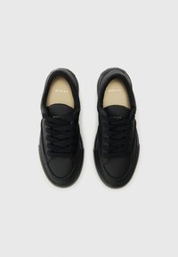 Mustad mustadest sneakerid siledast nahast pealmisega, ümmarguste paelte, ümmarguse varbaga ja tekstuurse kummitaldadega. Brändi logo on nähtav seest.